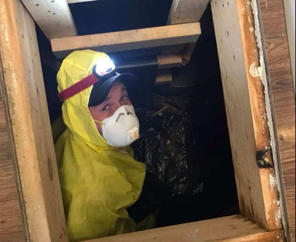 Technician in protective gear and a headlamp entering a crawlspace hatch