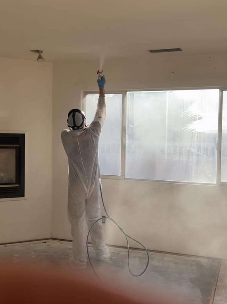 Technician in a protective suit spraying a ceiling in an empty room