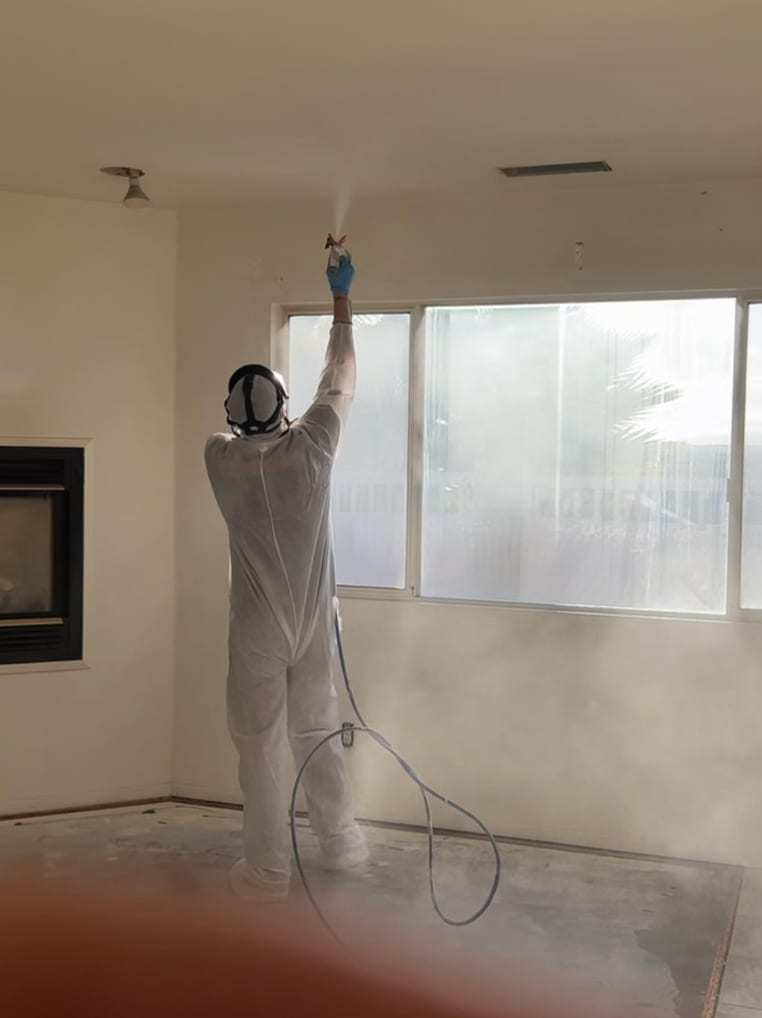 Technician in a protective suit spraying a ceiling in an empty room