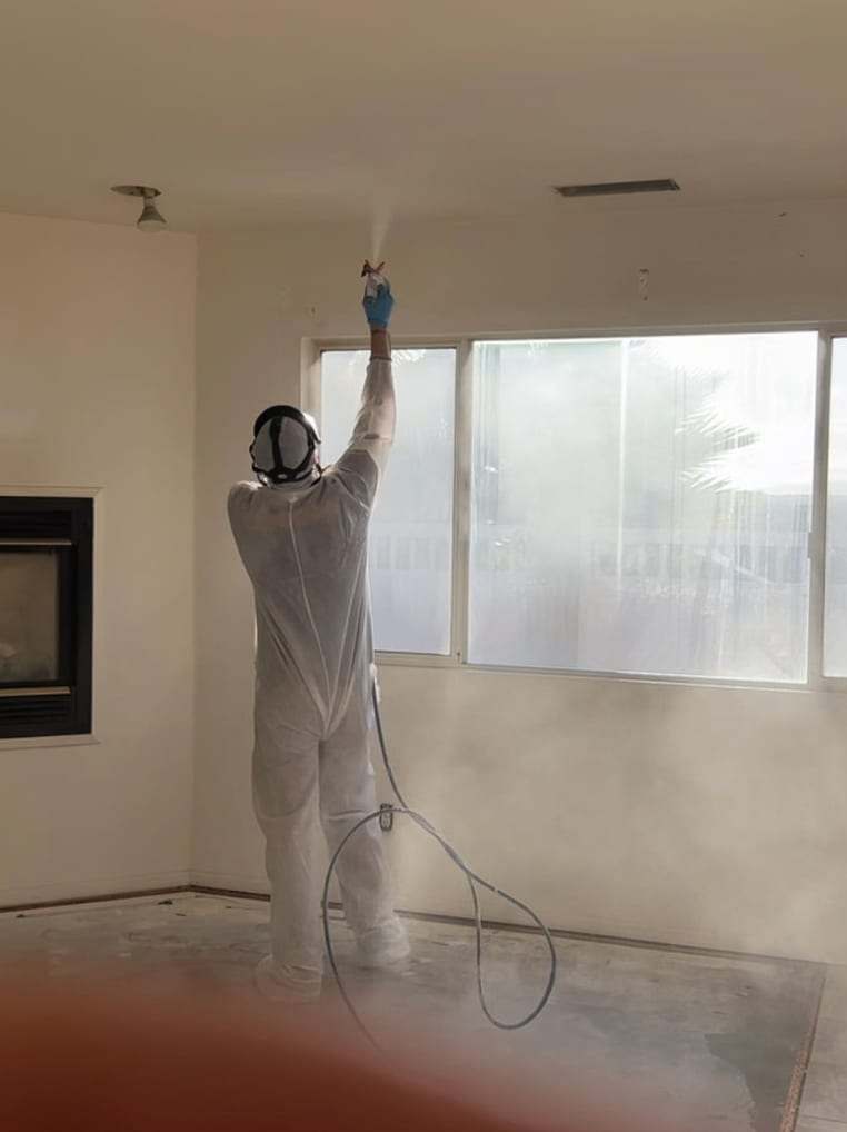 Technician in a protective suit spraying a ceiling in an empty room