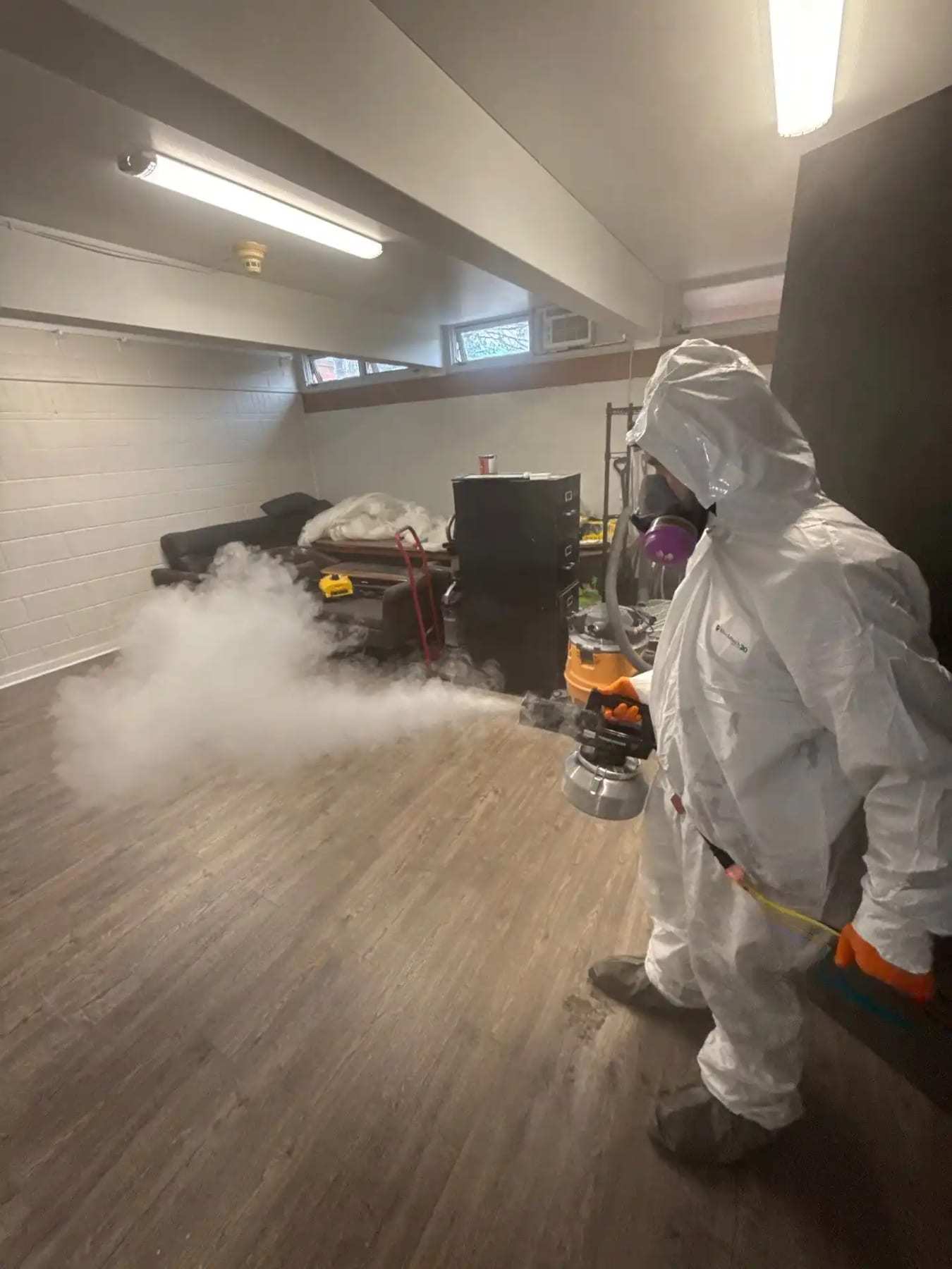Technician in a protective suit fogging a room with a thermal fogger