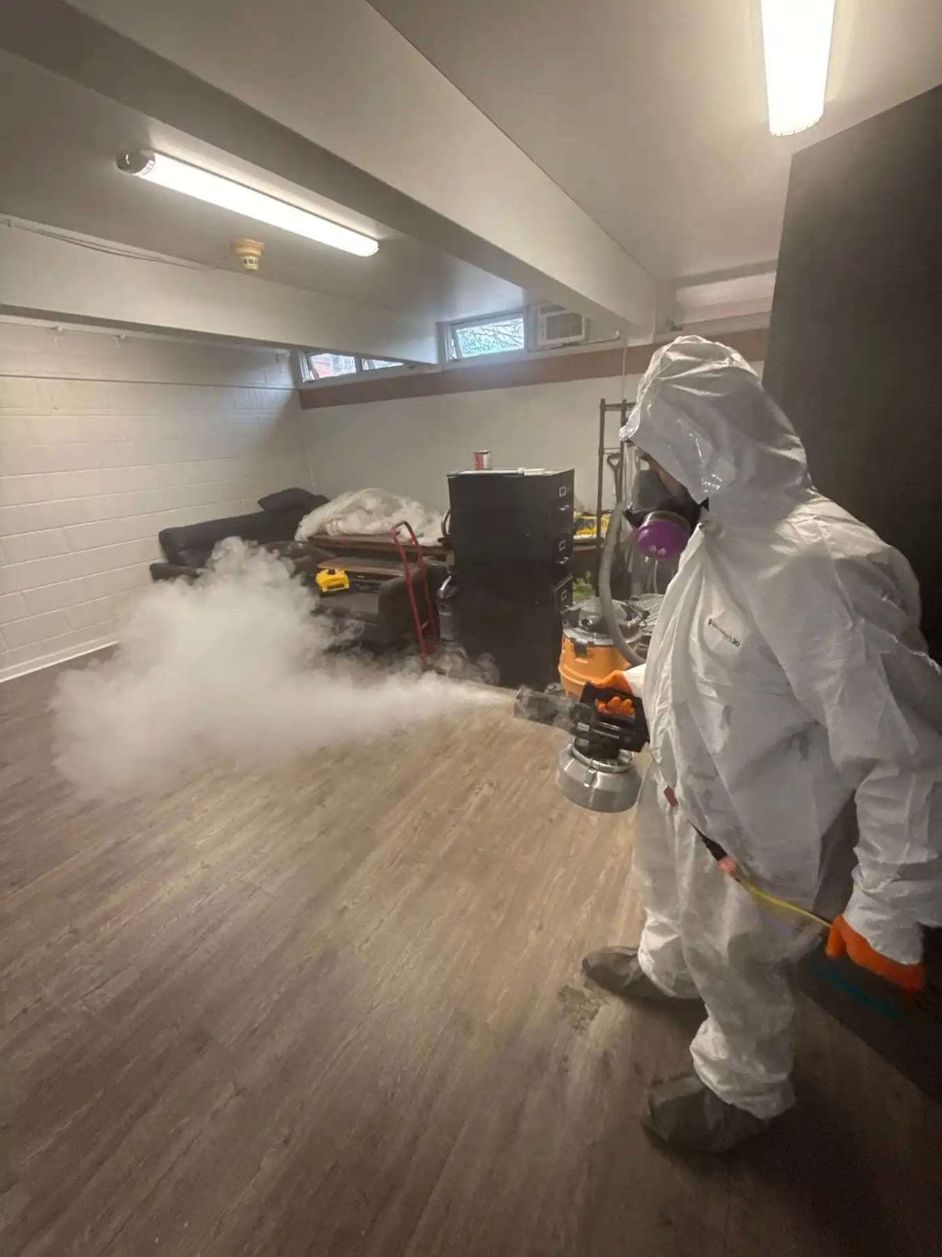 Technician in a protective suit fogging a room with a thermal fogger